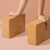 Two cork yoga blocks being held by hands on a beige background