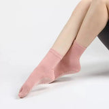 Pink socks with non-slip rubber dots down the bottom by a person on a light grey background
