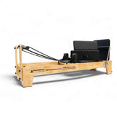 Wooden Pilates Reformer PL-600 with black cushions and resistance springs on white background