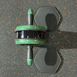 A green and black ab roller exercise wheel with a black textured carrying strap, shown from a top-down perspective on a dark gray speckled gym floor.