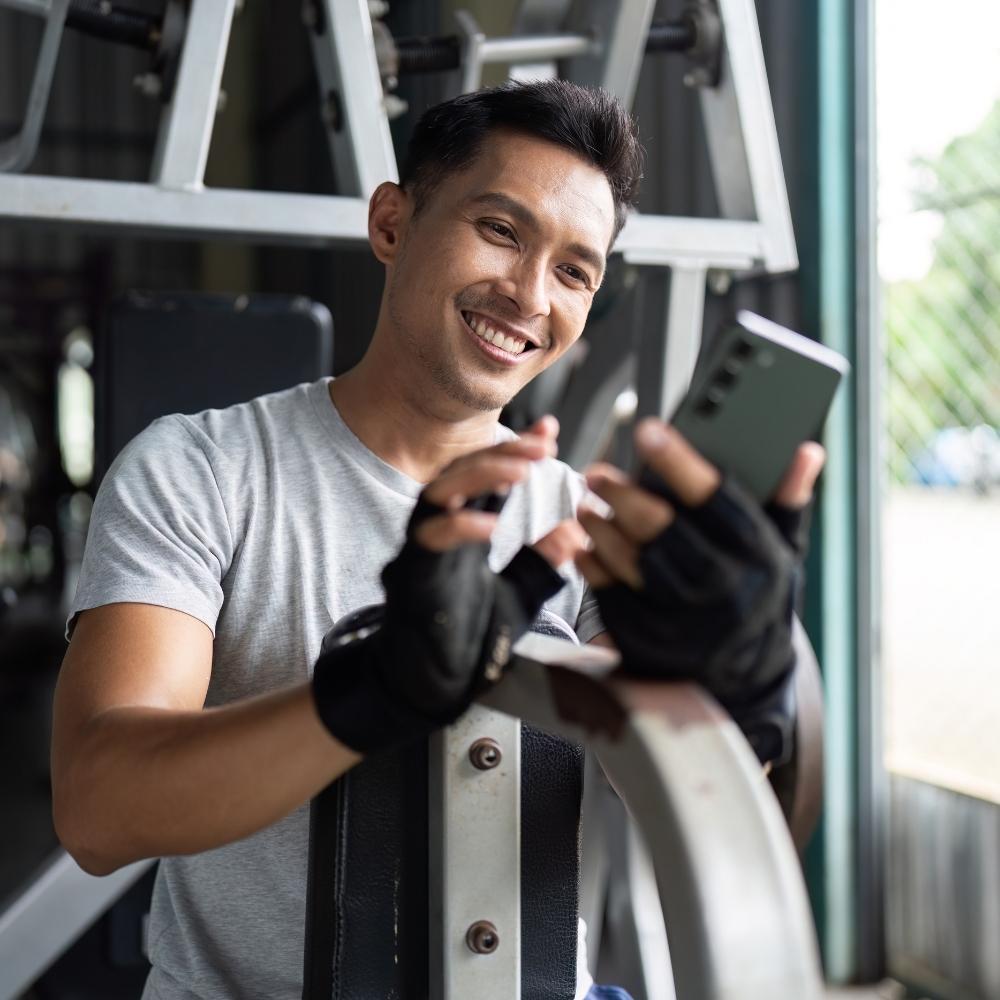 Man in a gym setting with exercise equipment, wearing gloves and smiling.
